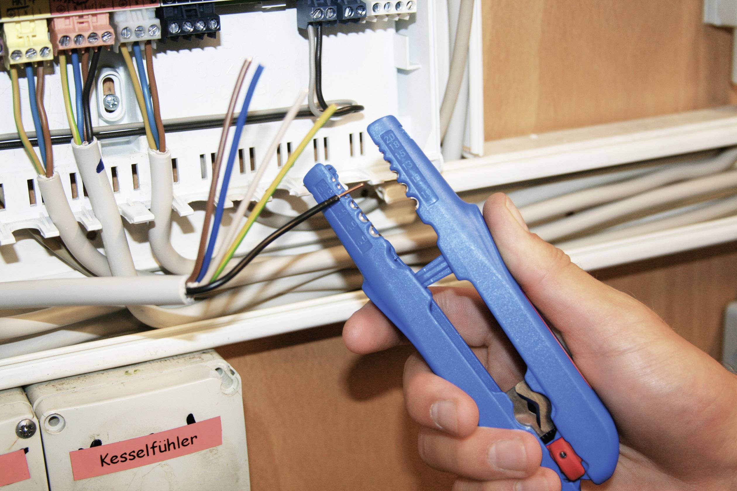 Eine Person verbindet Kabel mit einem blauen Kabelschneider in einem Verteilerkasten.