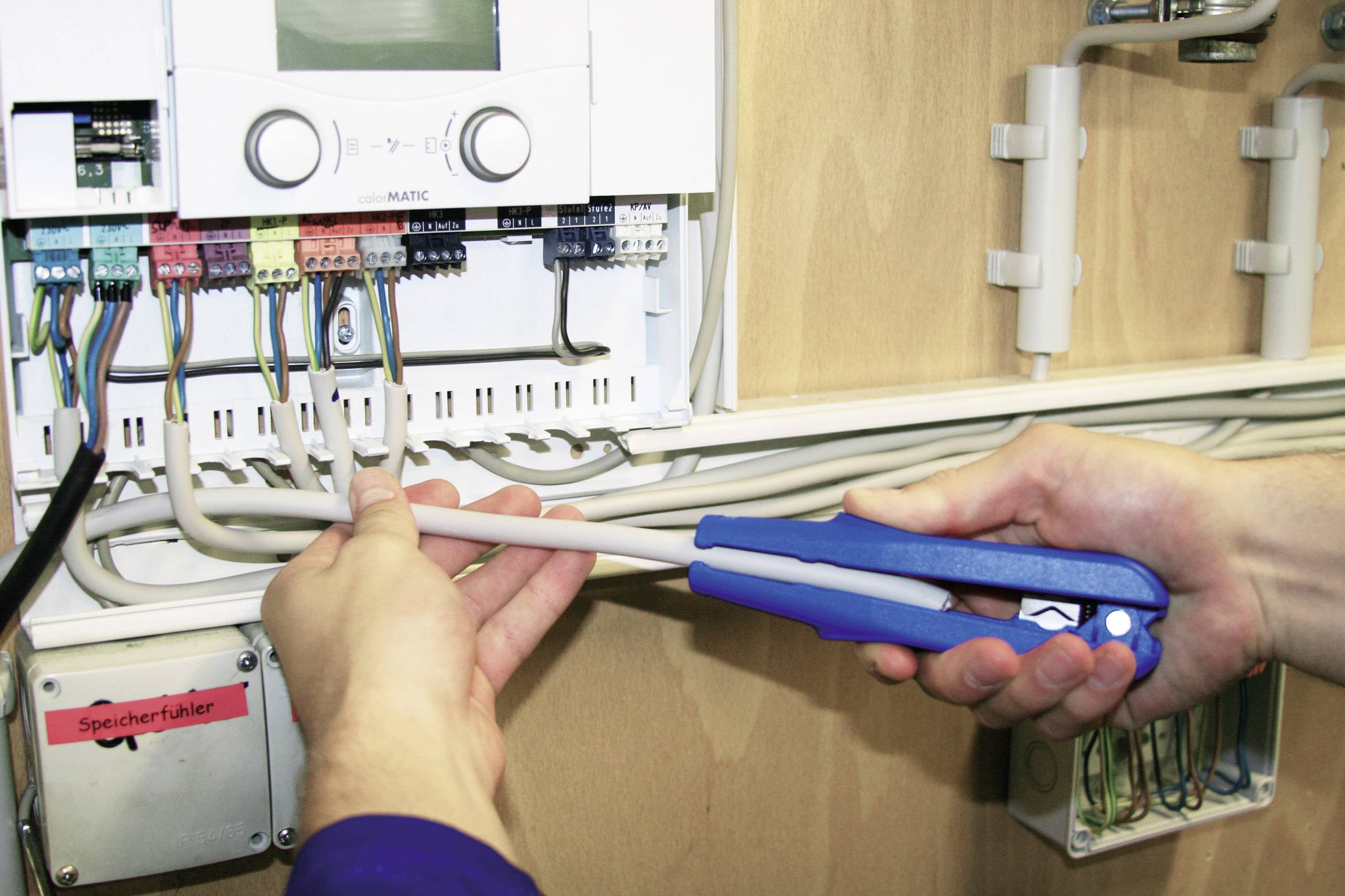 Zwei Hände arbeiten an einem elektrischen Verteilerkasten mit Kabeln und Werkzeug. Eine rote Box beschriftet mit 'Speicherfühler' ist sichtbar.