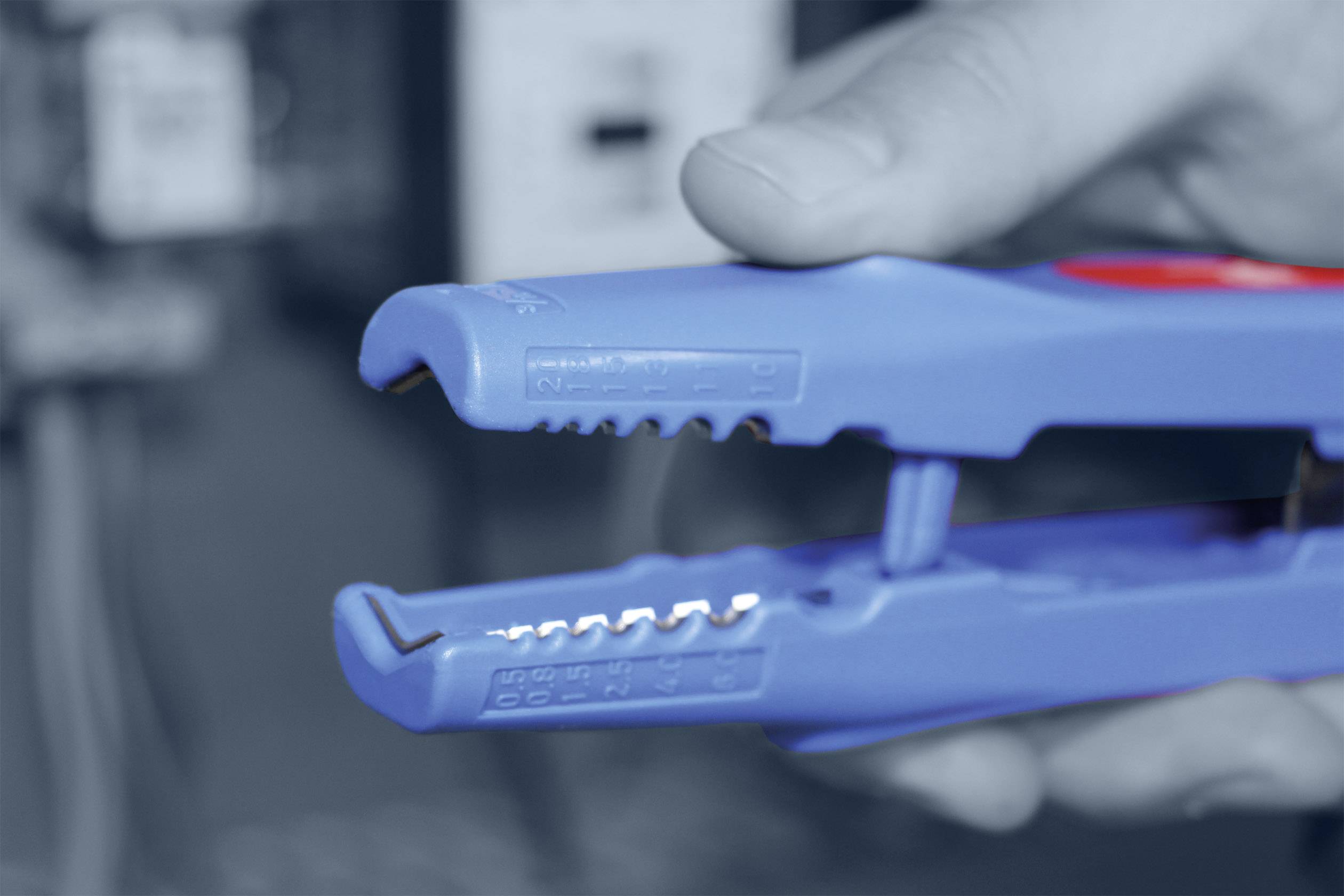 Eine Hand hält eine blaue Abisolierzange, die in Nahaufnahme gezeigt wird.
