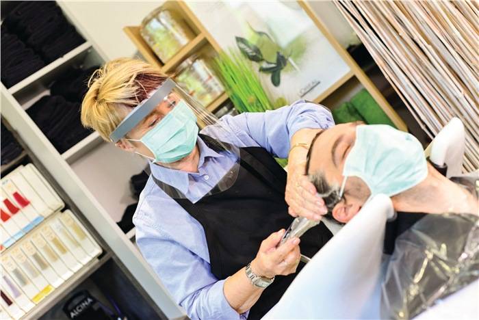 Hair-Stylistin im Einsatz. Sie wäscht die Haare eines Kunden und trägt dabei Gesichtsschutz und Atemmaske.