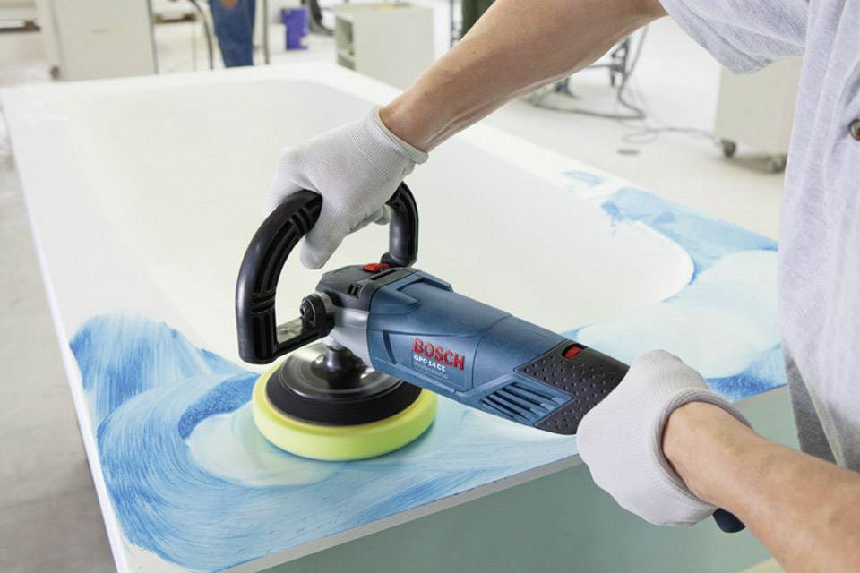 Eine Person poliert mit einer Bosch-Poliermaschine eine weiß-blaue Oberfläche in einer Werkstatt.