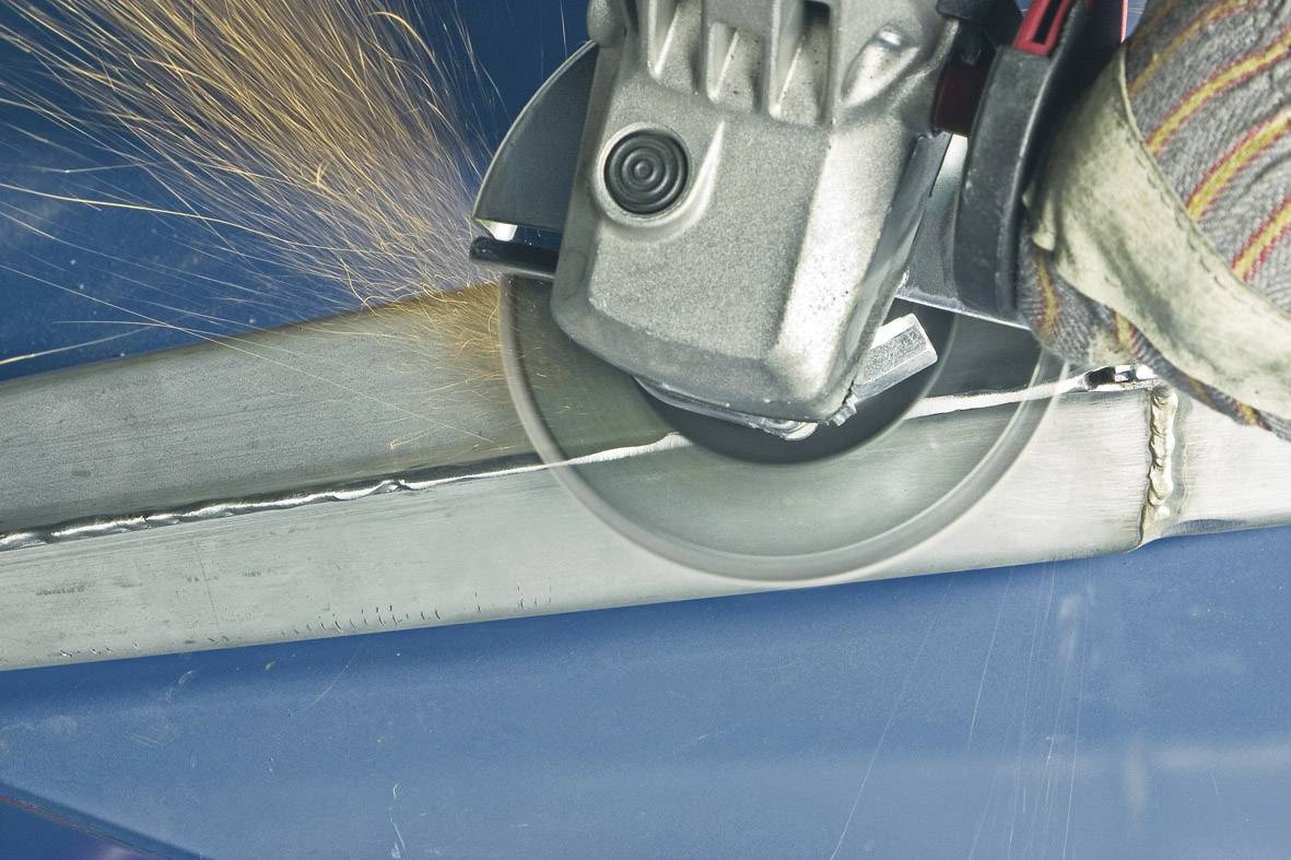 Eine Schleifmaschine bearbeitet einen Metallbalken, es entstehen Funken. Eine Hand in Arbeitshandschuhen hält die Maschine fest.