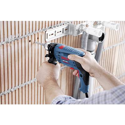 Eine Person bohrt mit einer blauen und schwarzen elektrischen Bohrmaschine ein Loch in eine rot-weiße Ziegelwand.
