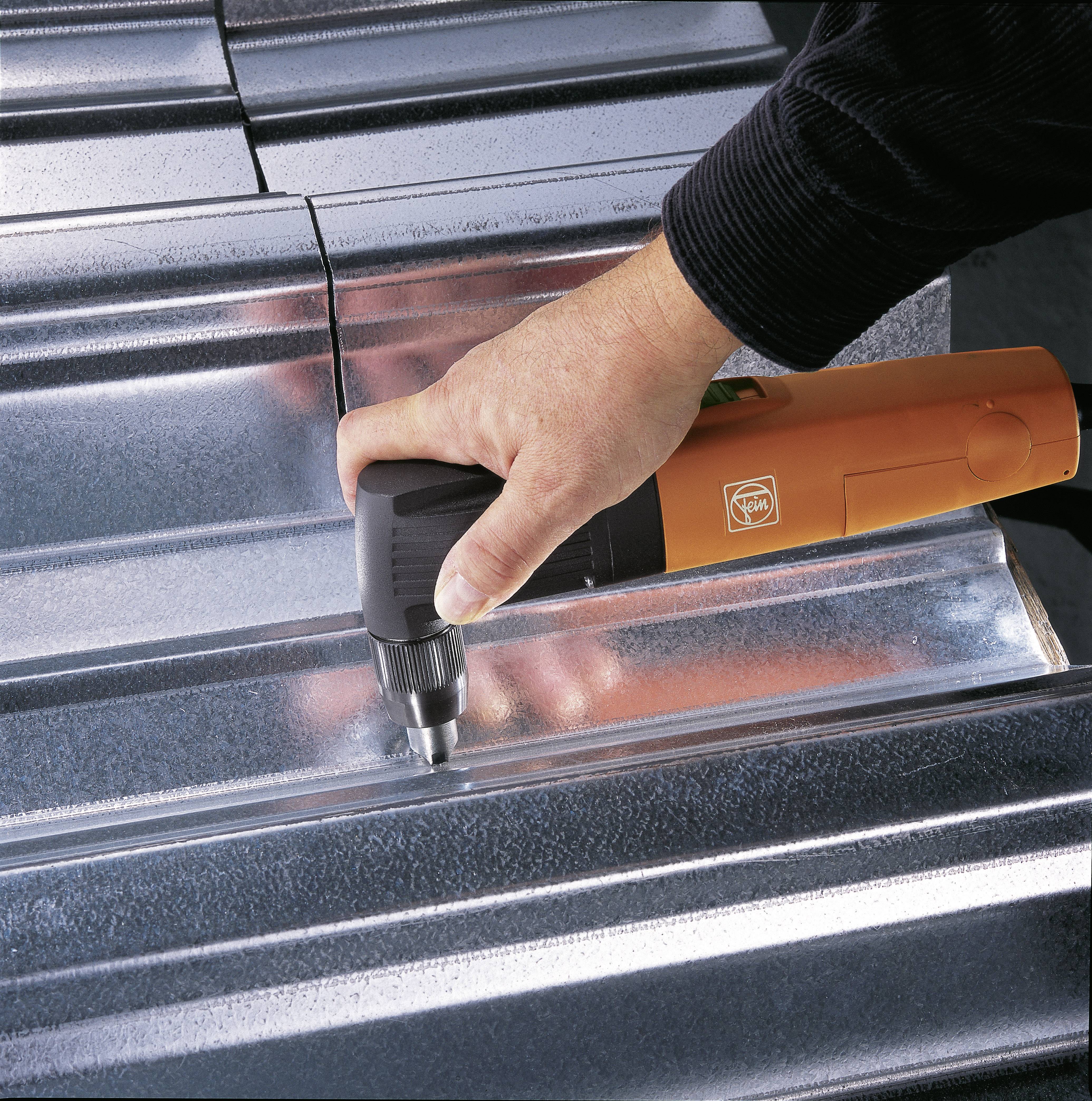 Eine Person verwendet ein orangefarbenes Elektrowerkzeug, um eine silberne Metalloberfläche zu bearbeiten.