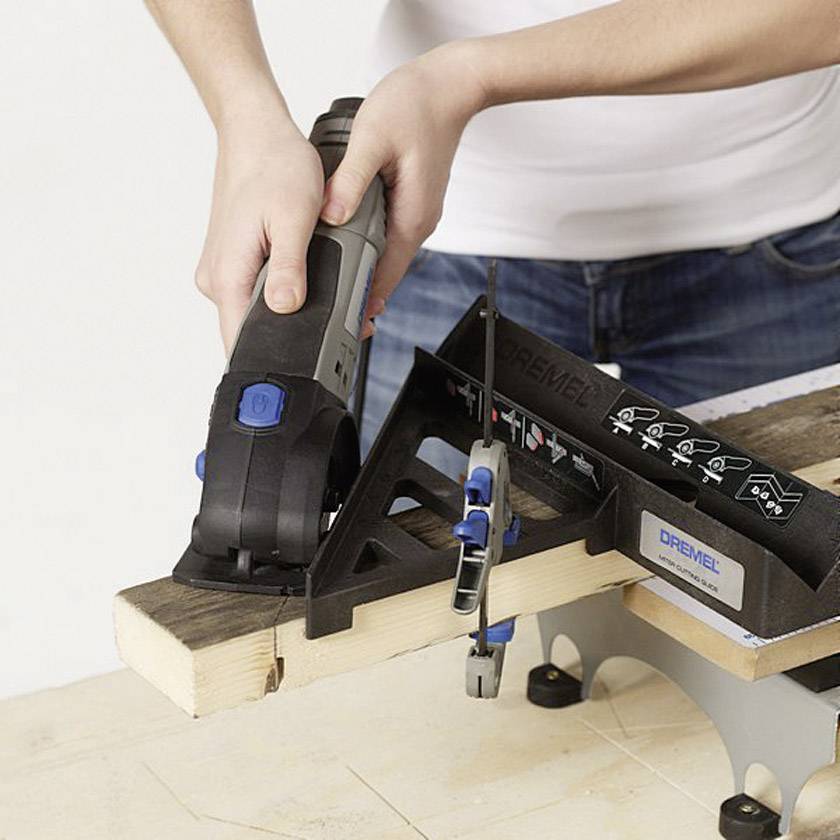 Person sägt ein Holzstück mit einem Elektrowerkzeug. Ein Winkelhalter fixiert das Holz. Sicheres Arbeiten wird demonstriert.