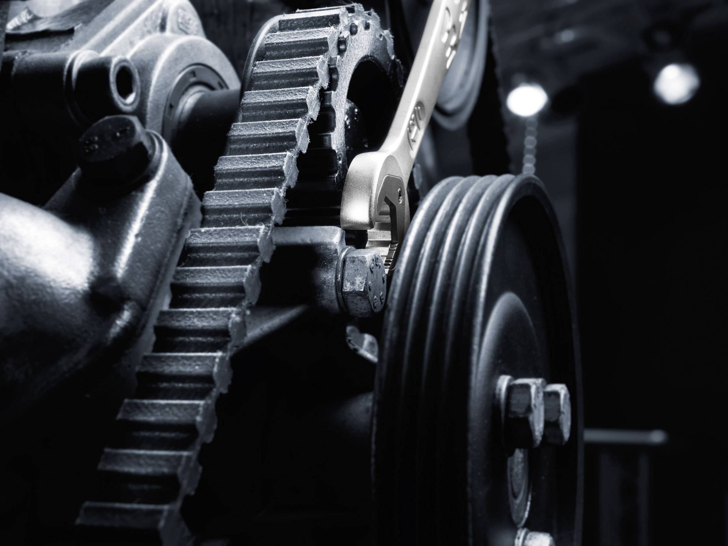 Ein Schraubenschlüssel justiert eine große, industrieähnliche Maschine mit Zahnrädern und Riemenscheiben in einer Werkstattumgebung.