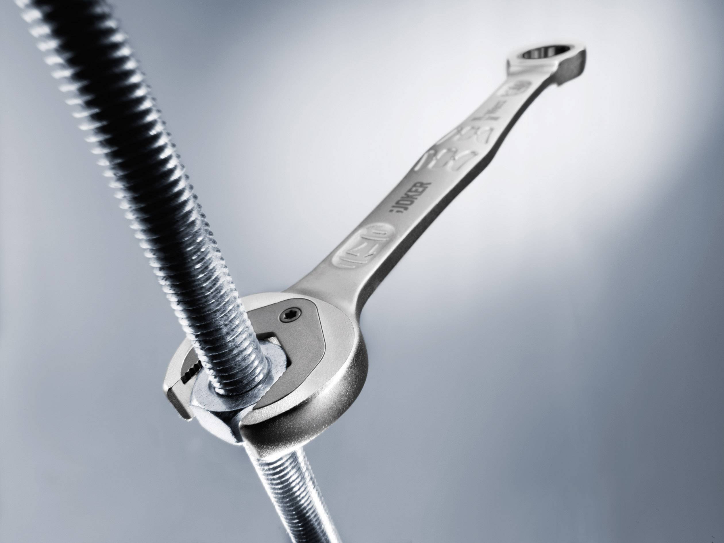 Ein Schraubenschlüssel zieht eine Schraube an. Die metallische Oberfläche reflektiert Licht, was auf mechanische Arbeit hindeutet.