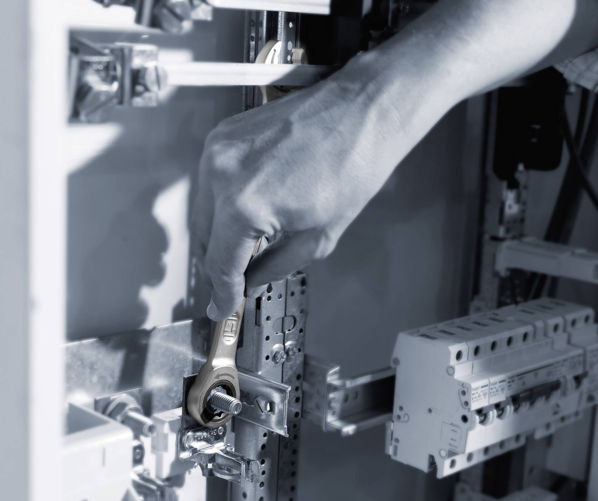 Eine Hand hält einen Schraubenschlüssel und arbeitet an einem elektrischen Schaltkasten. Fokus auf Feineinstellung oder Wartung.