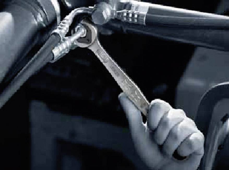 Hand hält einen Schraubenschlüssel, der an einer Metallverbindung in einem technischen oder industriellen Umfeld arbeitet.