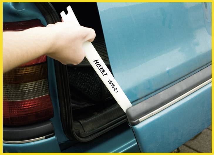 'Eine Hand nutzt ein Kunststoff-Keilwerkzeug, um die Rücklichter eines blauen Autos abzunehmen. Das Werkzeug trägt die Aufschrift "HAZET 1965-21".'
