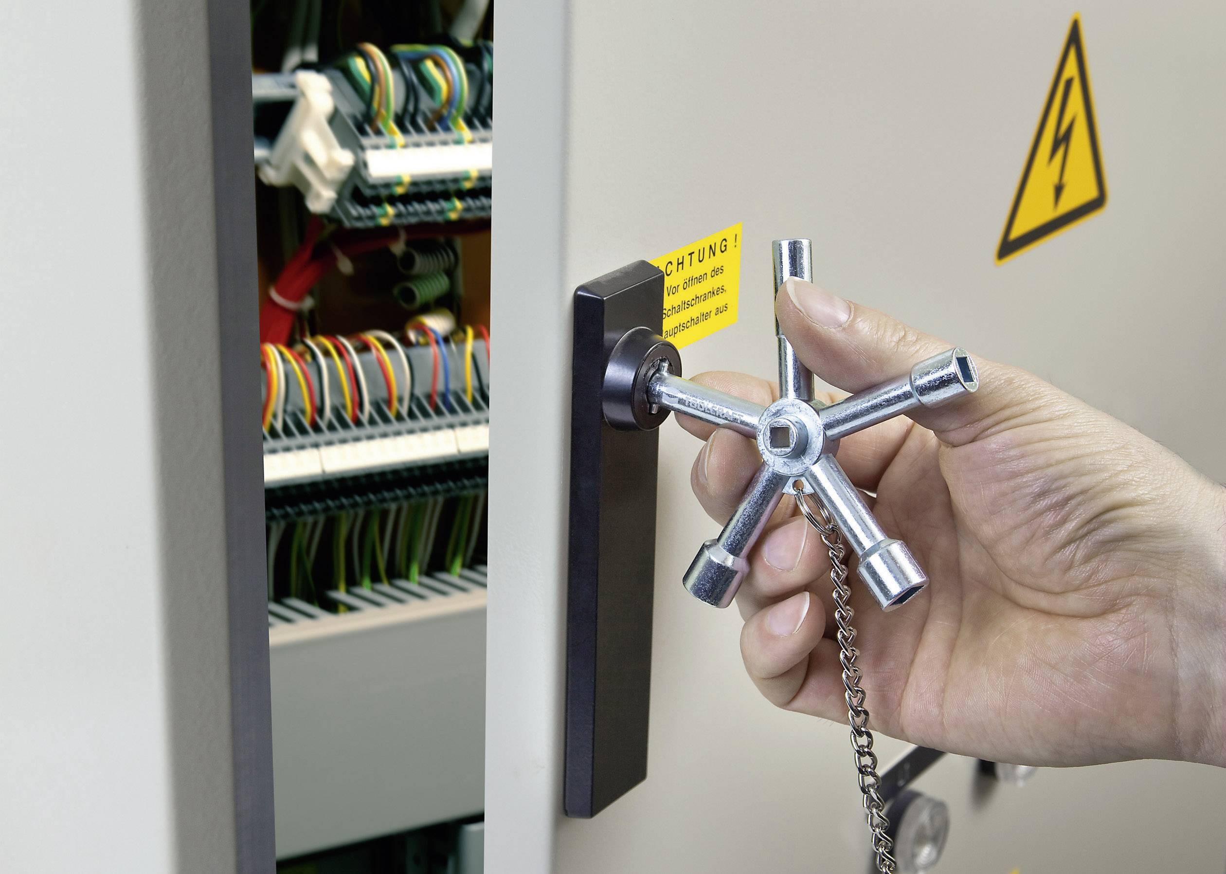Eine Hand öffnet mit einem Spezialschlüssel einen Schaltschrank. Im Hintergrund sind bunte Drähte und ein Warnsymbol zu sehen.