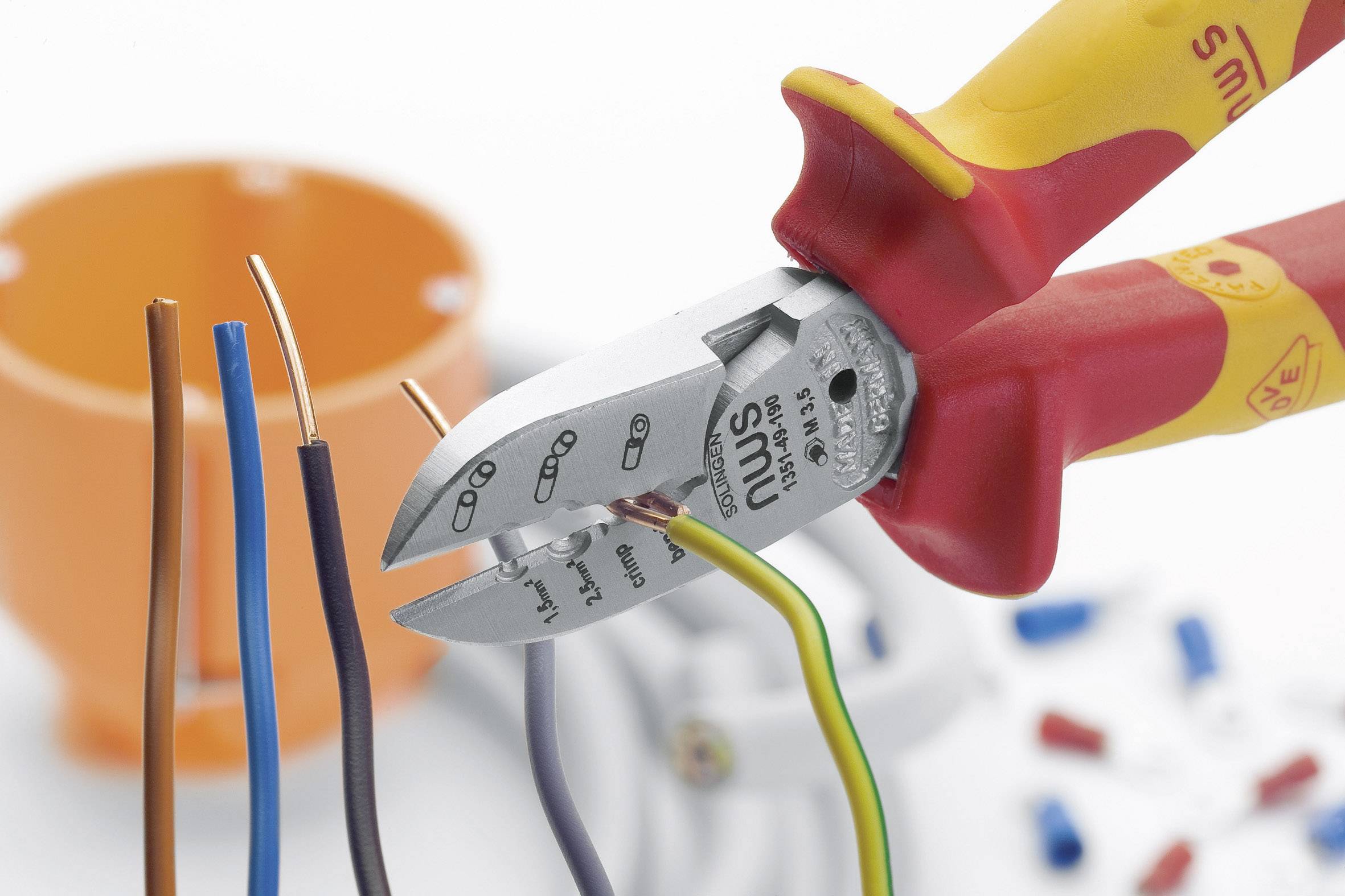 Seitenschneider durchtrennt bunte Kabel in Nahaufnahme. Im Hintergrund unscharfe Kabelklemme und Kabelmantel. Hauptfokus auf Werkzeug.