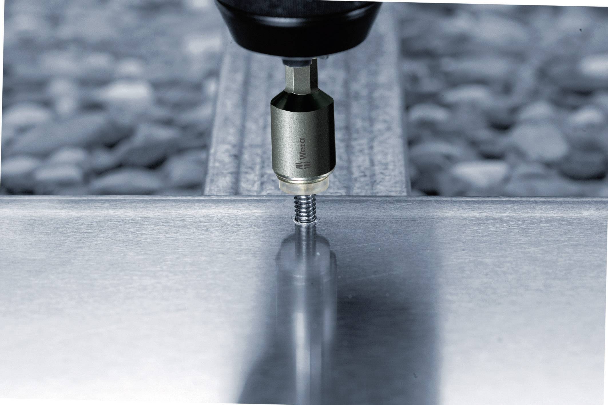 Maschine schraubt Bolzen in Metallplatte. Nahaufnahme. Hintergrund unscharf. Aktion industrieller Prozess.