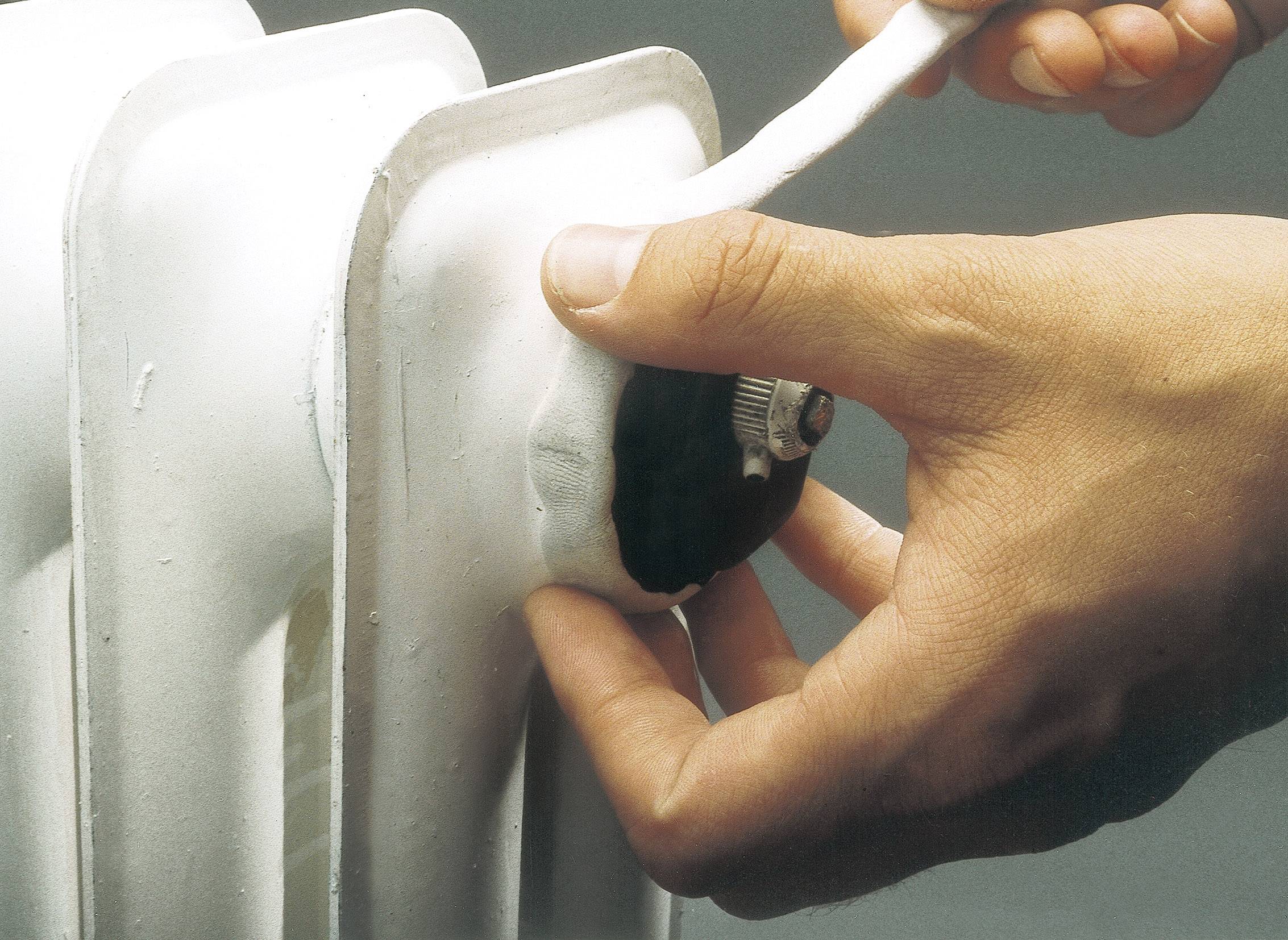 Eine Hand dreht ein Ventil an einem weißen Heizkörper. Eine andere Hand hält Isoliermaterial.