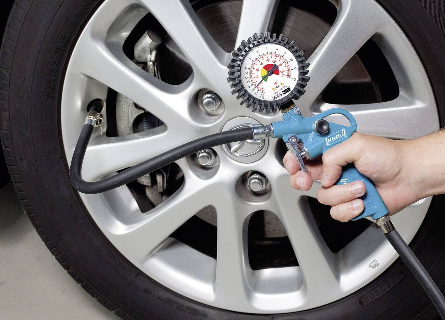 Eine Person misst den Luftdruck eines Autoreifens mit einem runden Messgerät und einer blauen Druckluftpistole.