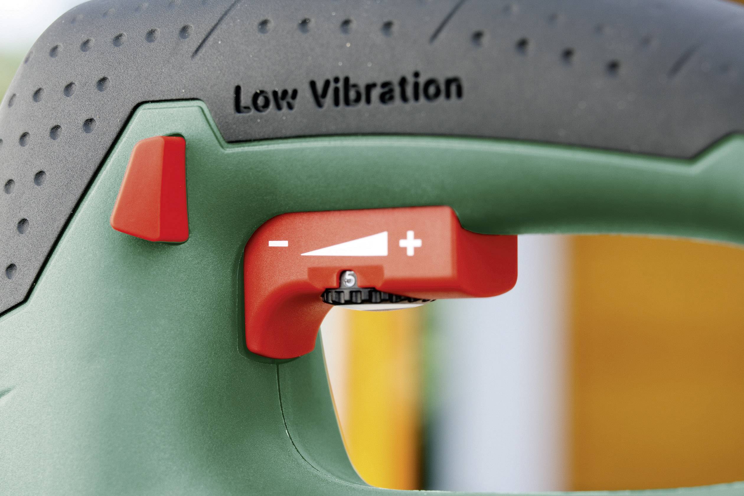 Nahaufnahme eines grünen Werkzeugs mit rotem Schalter, Beschriftung 'Low Vibration' und Regler mit Symbolen für Minus und Plus zur Einstellung der Vibrationsintensität.