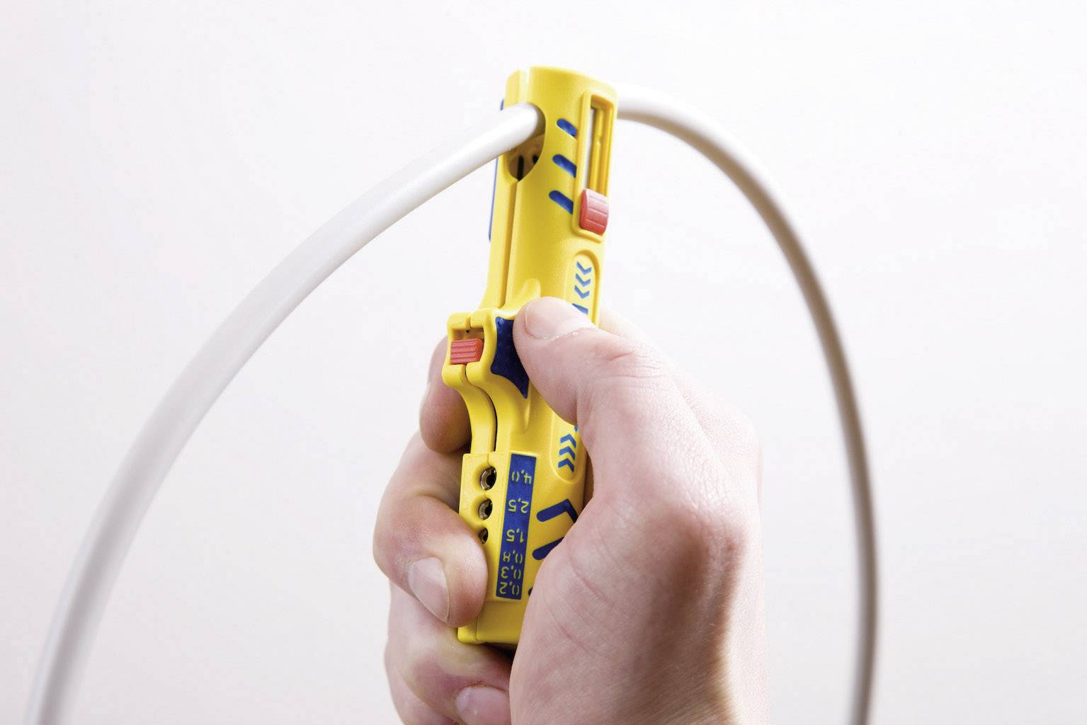 Eine Hand hält ein gelbes Werkzeug, das ein weißes Kabel abisoliert. Das Werkzeug hat blaue und rote Markierungen.