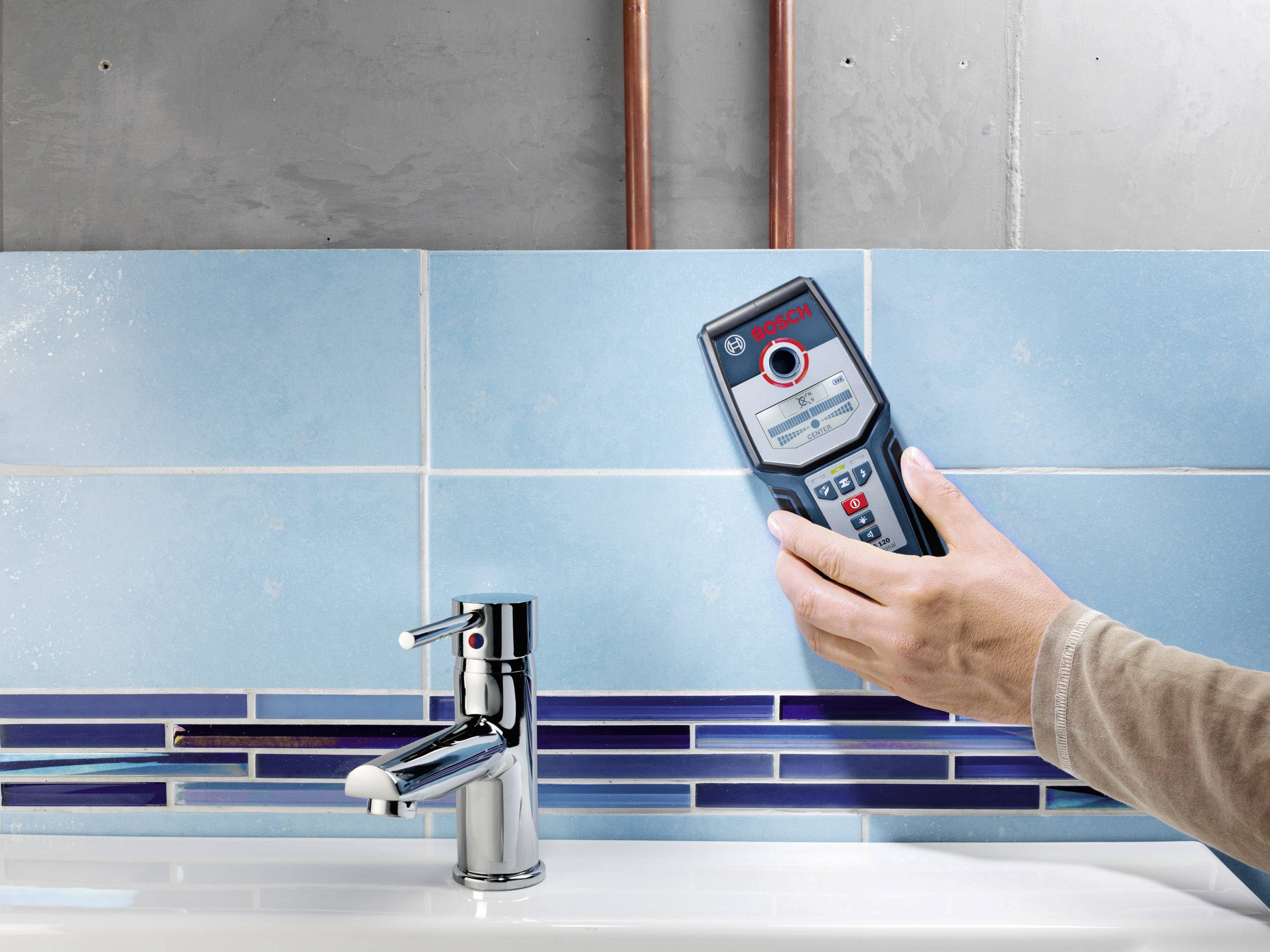 Eine Person hält ein Bosch-Entfernungsmessgerät in der Hand und misst den Abstand zu einem Wasserhahn vor einer gefliesten Wand.