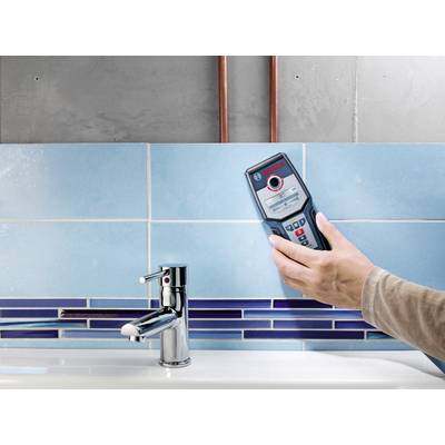 Eine Person hält ein Bosch-Entfernungsmessgerät in der Hand und misst den Abstand zu einem Wasserhahn vor einer gefliesten Wand.