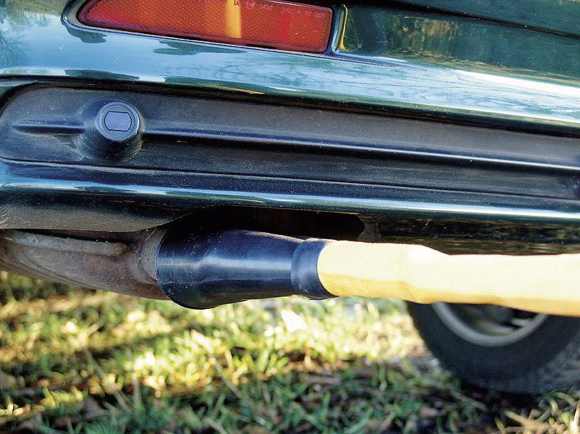 Ein gelber Schlauch ist mit dem Auspuff eines grünen Autos verbunden. Dies deutet auf eine Abgasuntersuchung oder Emissionskontrolle hin.