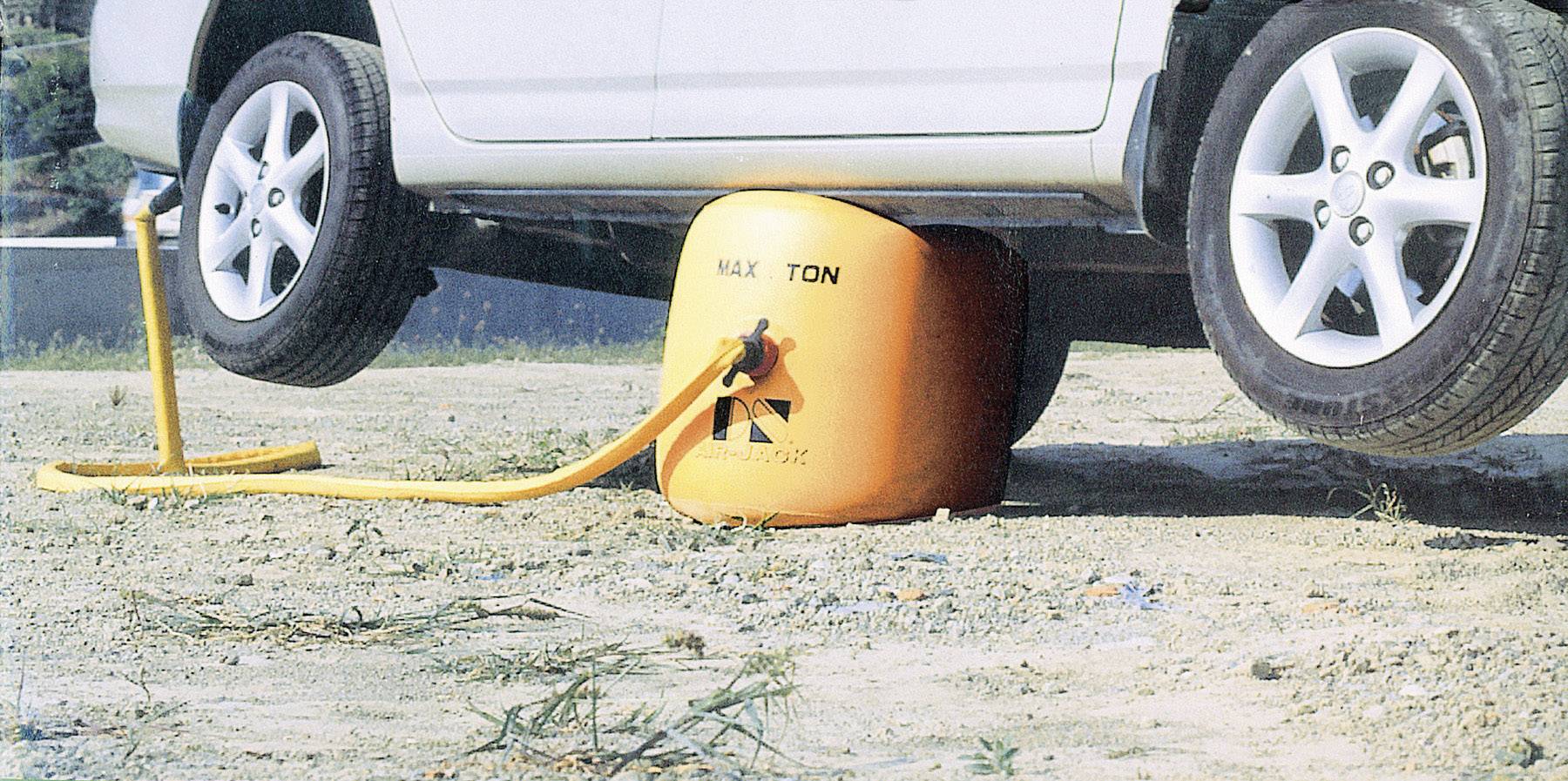 Ein Auto wird von einem aufblasbaren Luftkissen angehoben, das an einem Luftschlauch angeschlossen ist, auf einer sandigen Oberfläche.
