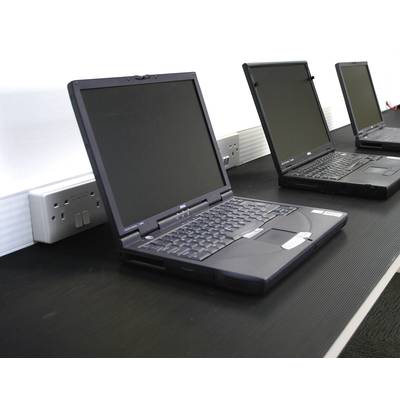 Drei geöffnete Laptops auf einem Tisch mit Steckdosen im Hintergrund, die einsatzbereit erscheinen.