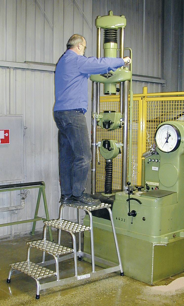 Ein Mann steht auf einer Trittleiter und bedient eine große grüne Maschine in einer industriellen Umgebung.