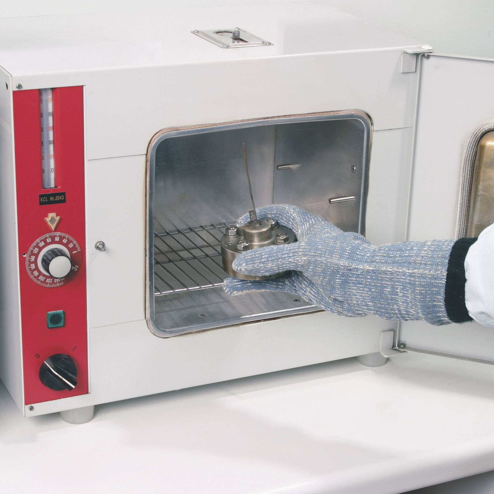 Eine Person mit Handschuhen platziert eine Metallprobe in einem geöffneten Labortrockenschrank.