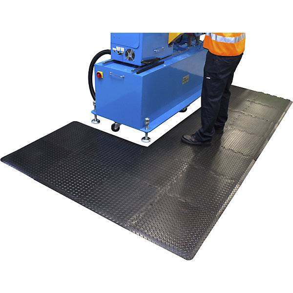 Ein Mann steht in einer Betriebshalle auf einer Anti-Ermüdungsmatte für die Bedienung einer Maschine.