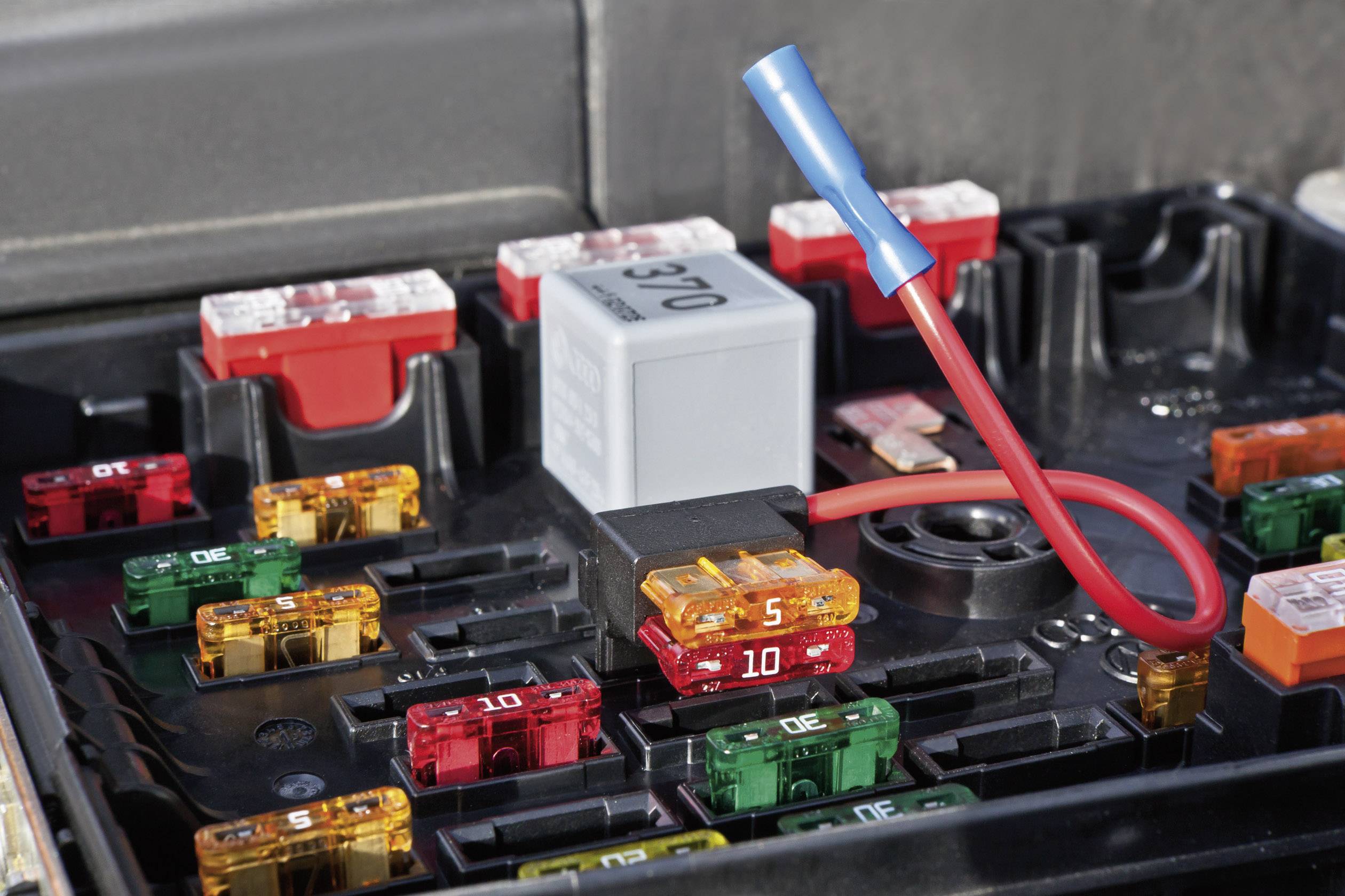 Mehrere farbige Autokraftstoffsicherungen in einer Sicherungsbox, ein rotes Kabel ragt heraus. Steckplatzbeschriftungen sichtbar.