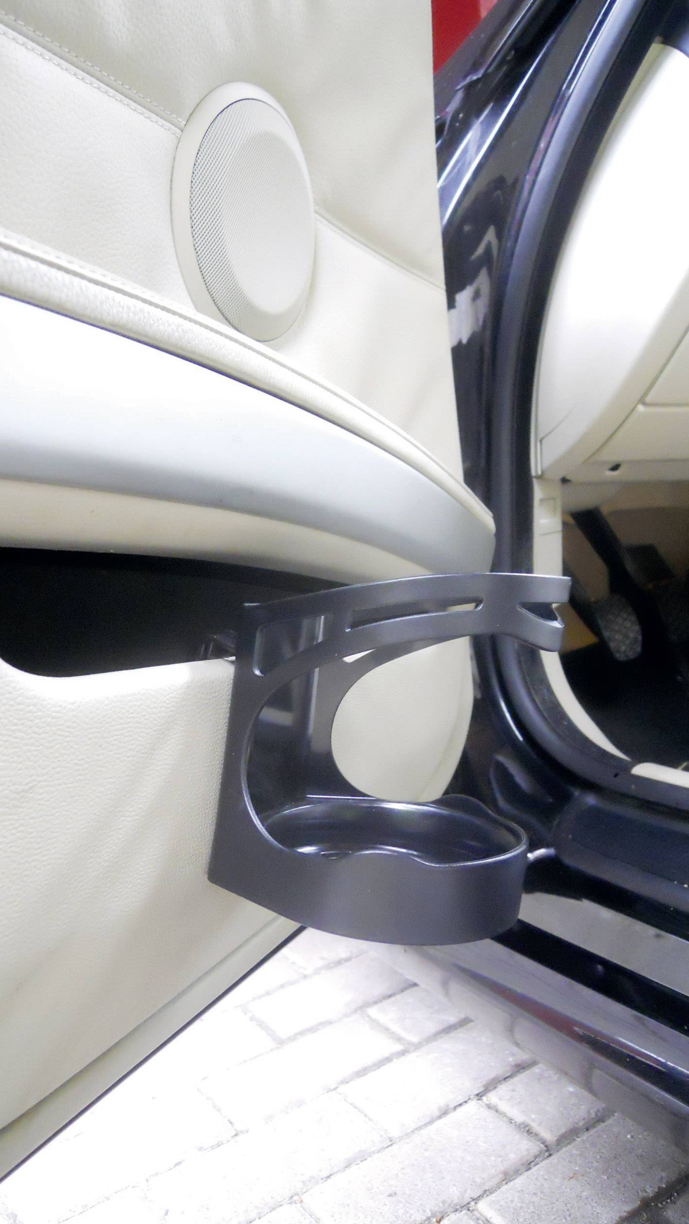 Schwarzer Klapp-Getränkehalter an der Innenseite einer Autotür montiert, neben hellbeiger Verkleidung und Lautsprecher.
