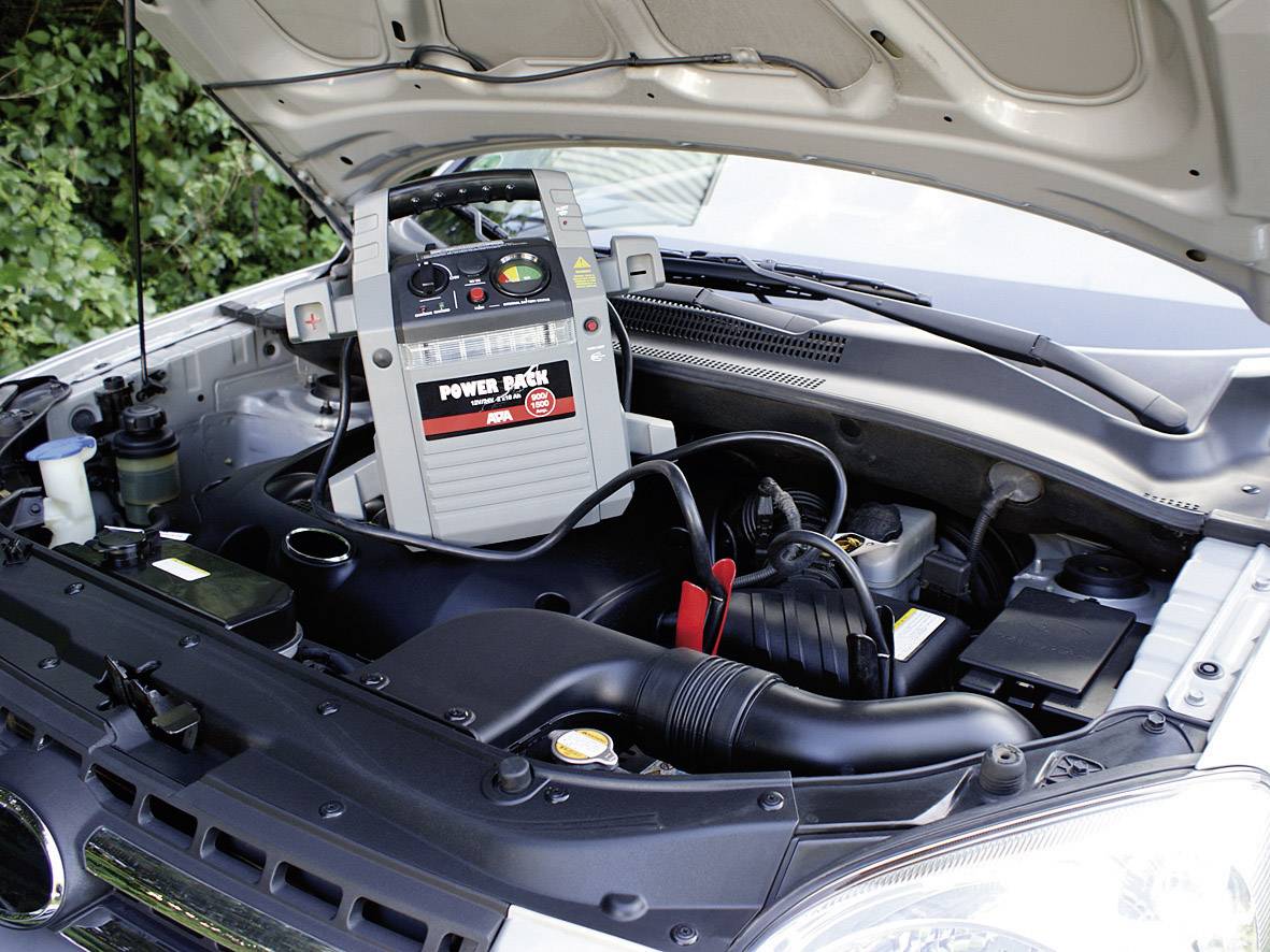 Autobatterie wird mit einem tragbaren Starthilfegerät im Motorraum aufgeladen.