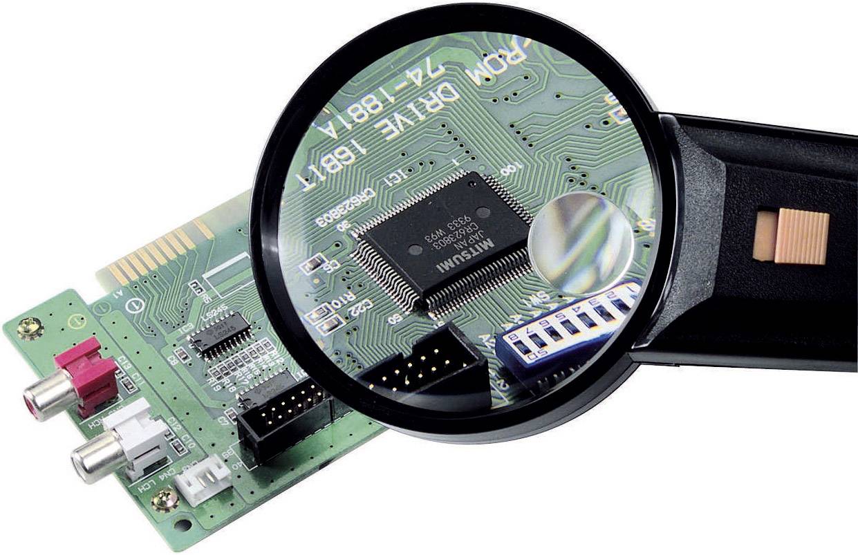 Eine Lupe vergrößert einen Mikrochip auf einer Computerplatine. Zu erkennen sind Schaltkreise und verschiedene elektronische Bauteile.