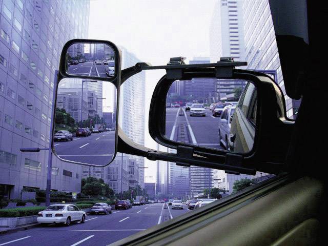 Blick aus einem Autofenster auf eine belebte Stadtstraße mit hohen Gebäuden. Rückspiegel zeigt den Verkehr hinter dem Auto.