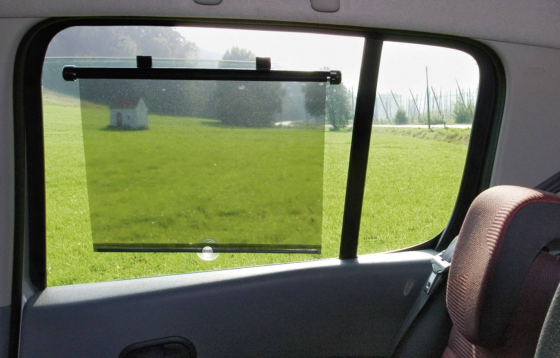 Auto-Innenansicht mit Blick durch das seitliche Autofenster auf ein grünes Feld und ein kleines weißes Haus in der Ferne.
