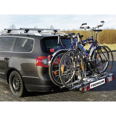 Silbernes Auto mit zwei Fahrrädern auf einem Fahrradträger am Heck, geparkt auf einem gepflasterten Platz bei Tageslicht.