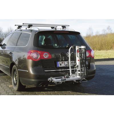 Ein dunkles Auto mit Dachgepäckträger hat ein metallisches Gestell am Heck befestigt. Es steht auf einem gepflasterten Platz.