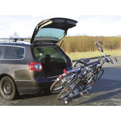 Ein offener Kombi-Kofferraum mit Fahrradträger und zwei Fahrrädern auf einem Parkplatz neben einer Wiese.