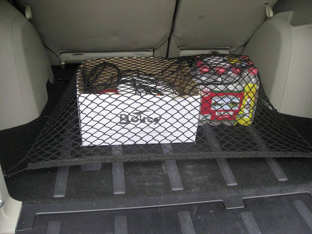 Kofferraum eines Autos mit Gepäcknetz, das eine Box und eine größere, rot-gelbe Batterie sichert.