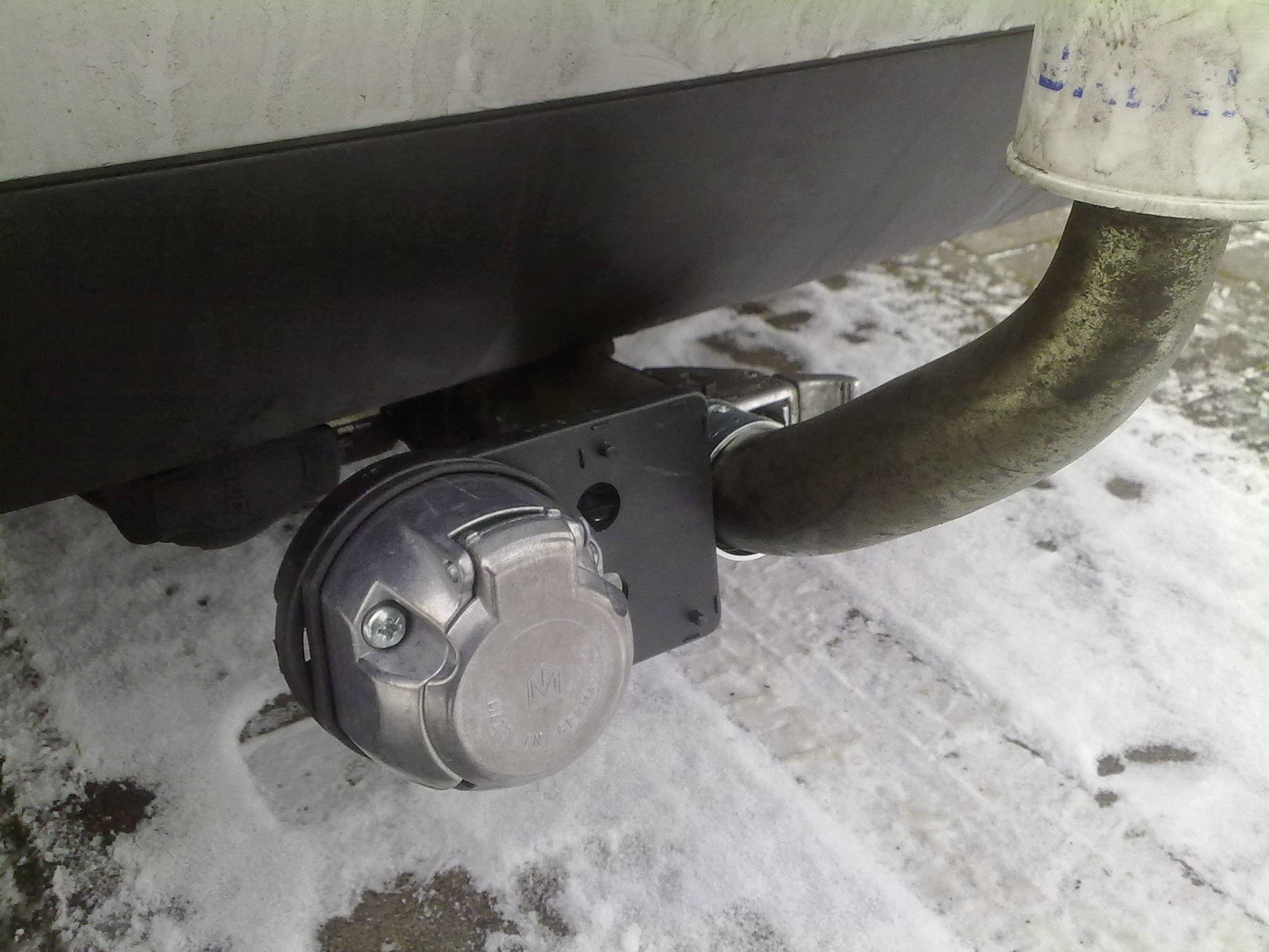 Abnehmbare Anhängerkupplung an einem Fahrzeug, montiert unter der Stoßstange, umgeben von schneebedecktem Boden.