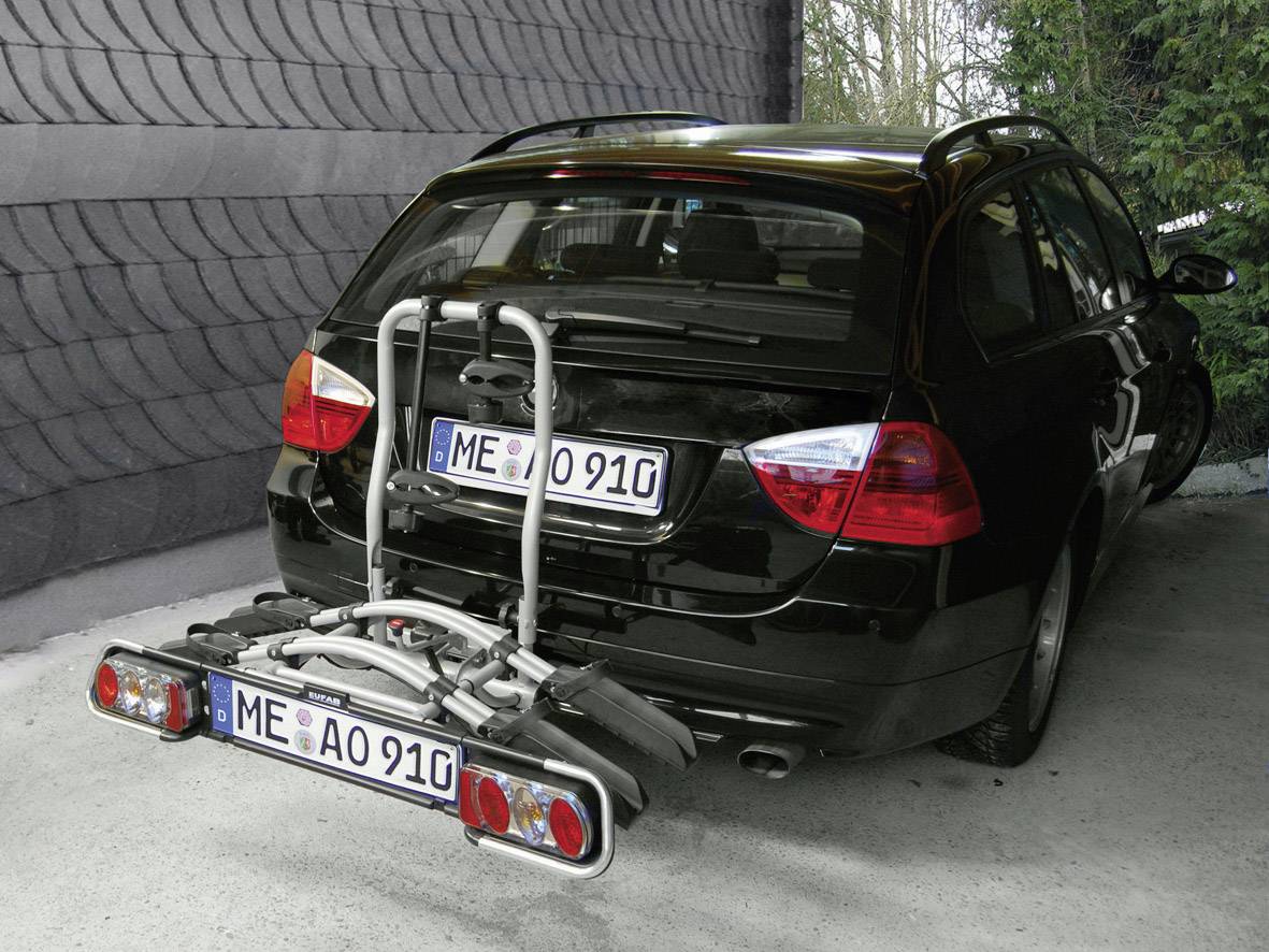 Schwarzes Auto mit Fahrradträger auf der Anhängerkupplung, geparkt in einer überdachten Zufahrt. Nummernschild sichtbar.