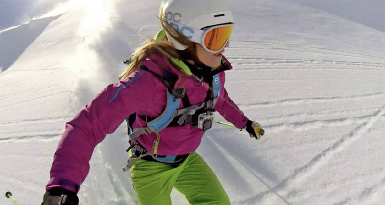 Eine Person in bunter Skiausrüstung fährt einen schneebedeckten Hang hinunter, umgeben von schneebedeckter Landschaft.