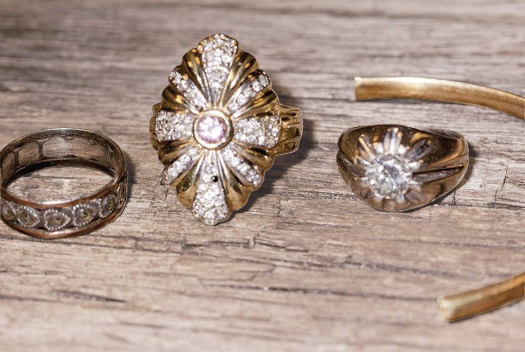 Drei elegante Ringe aus Gold mit Diamanten liegen auf einer Holzoberfläche. Einer hat ein florales Design, einer ist breit und schlicht, der dritte hat einen großen zentralen Stein.