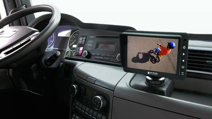 Die Kamera blickt auf das Cockpit eines Autos, in dem der zu einer Rückfahrkamera dazugehörige Bildschirm installiert ist. Die Kamera ist an und auf dem Monitor sieht man ein Kind, das Fahrrad fährt.