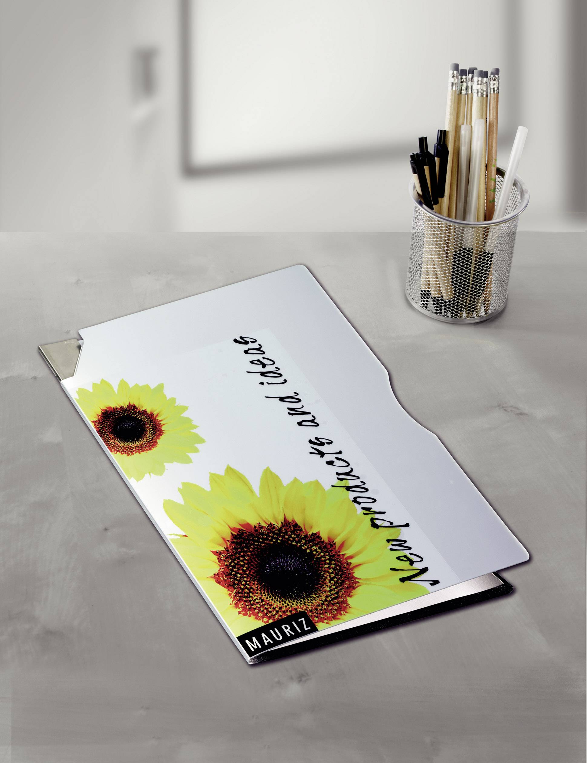 Kunststoffmappe mit Sonnenblumenmotiv auf Tisch, daneben Behälter mit Stiften. Text auf Mappe: 'New projects, new ideas'.