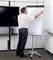 Ein Mann befestigt ein leeres Blatt Papier auf einem Flipchart in einem Konferenzraum mit einem Fernseher im Hintergrund.