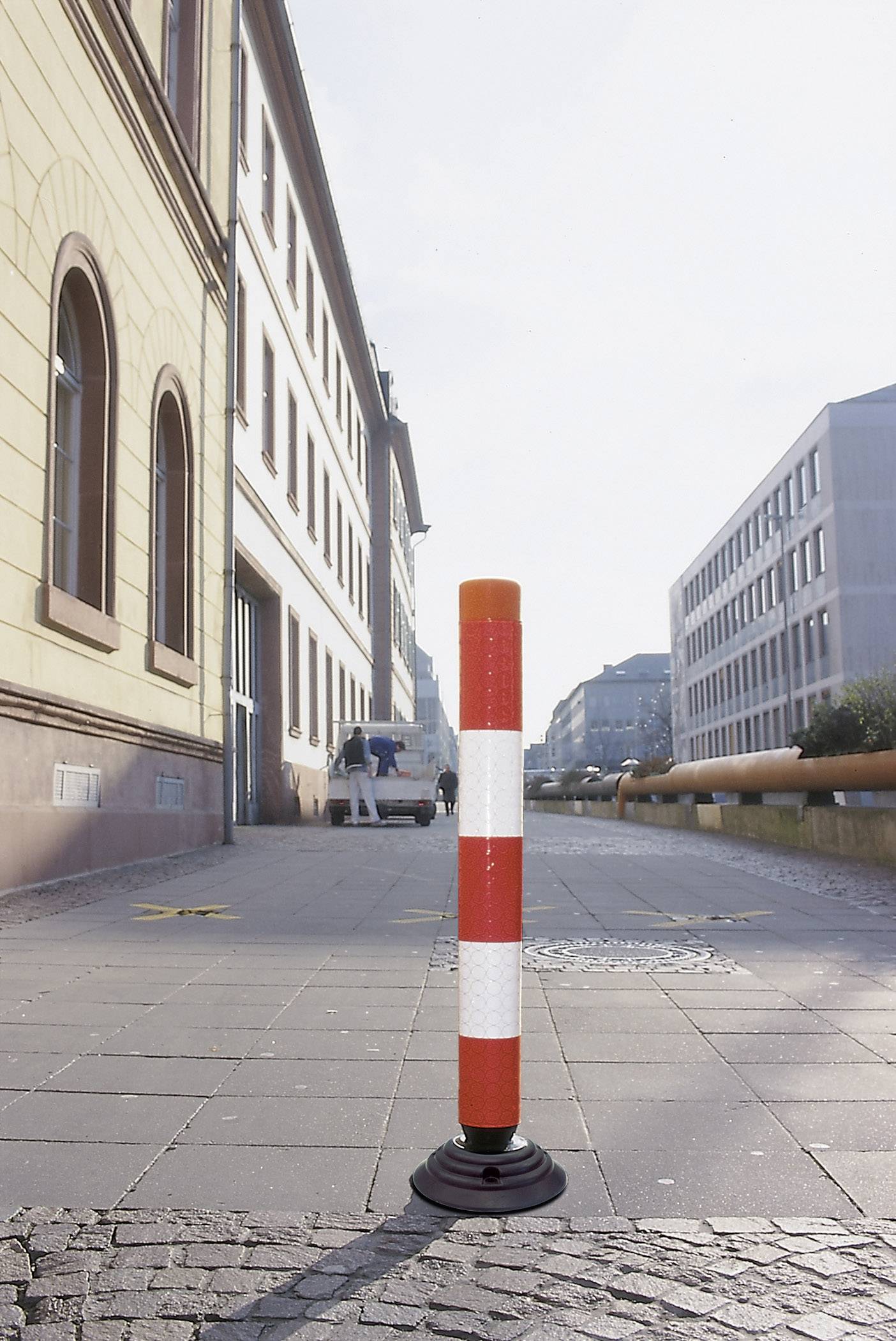 Ein rot-weiß gestreifter Poller steht auf einem Gehweg in einer städtischen Umgebung, um den Zugang zu regulieren.