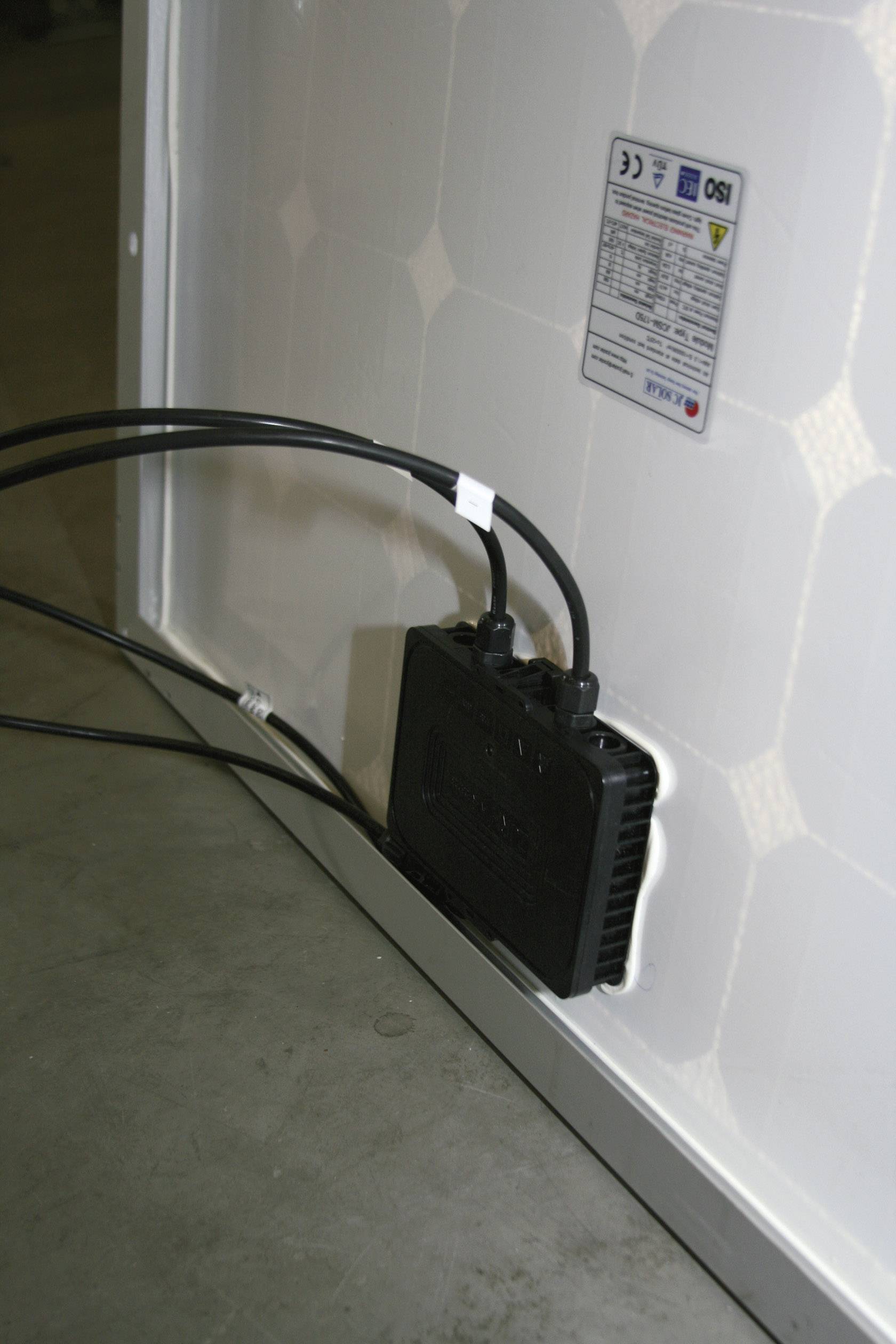 Rückseite eines Solarmoduls mit Anschlusskasten und angeschlossenen Kabeln; Etikett mit technischen Daten oben rechts sichtbar.
