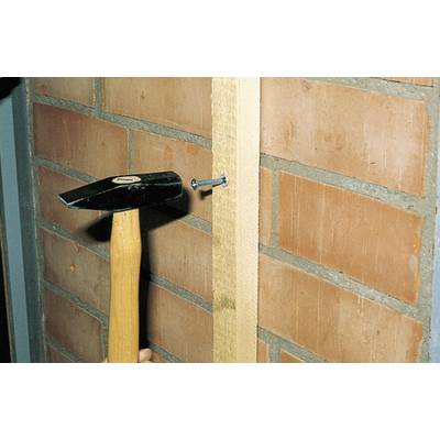 Ein Hammer schlägt einen Nagel in ein Holzbrett, das an einer Ziegelwand befestigt ist.