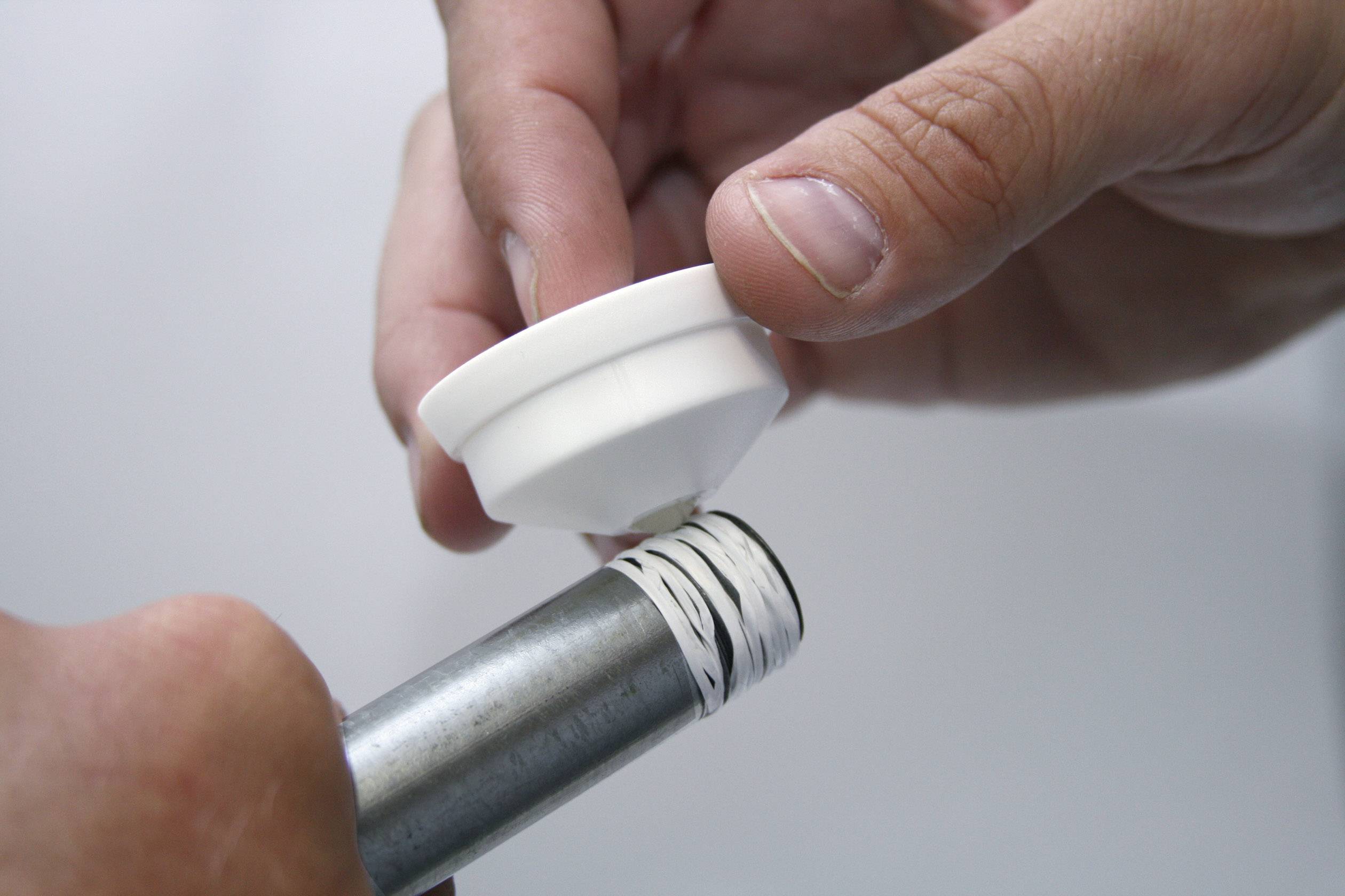 Nahaufnahme von zwei Händen, die weißes Dichtband um ein Metallrohr wickeln, um eine weiße Dichtung zu befestigen.